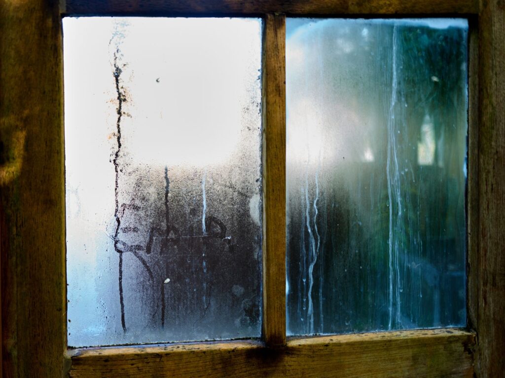 Condensation running down the glass of an old wooden-framed window