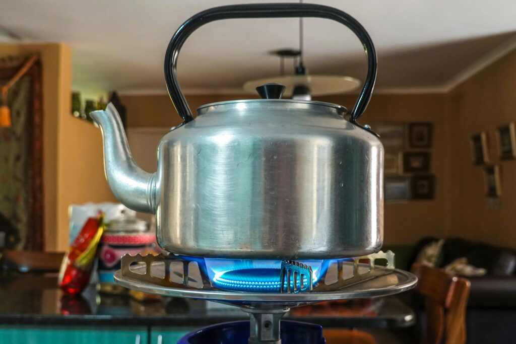 Close-up of a stainless steel kettle heating on a gas stove in a cozy kitchen setting.