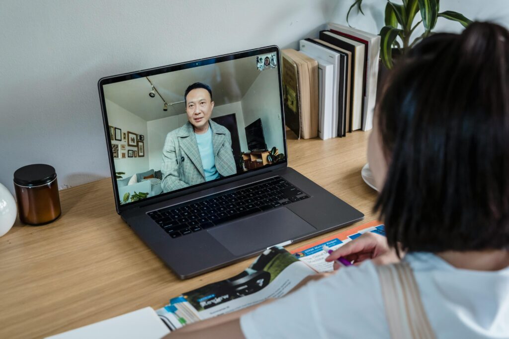 A woman engages in a video call on her laptop while sitting at a wooden desk indoors.