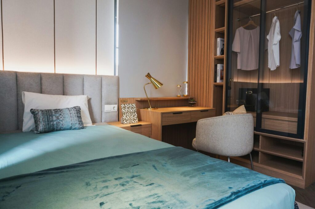 Stylish modern bedroom featuring a comfortable bed, wooden desk, and wardrobe with hanging clothes.