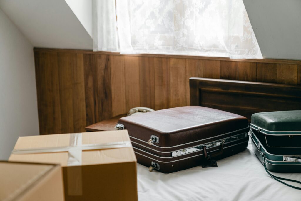 From above of brown and green vintage suitcases and packed carton boxes placed on bed with sheet in light room with slop