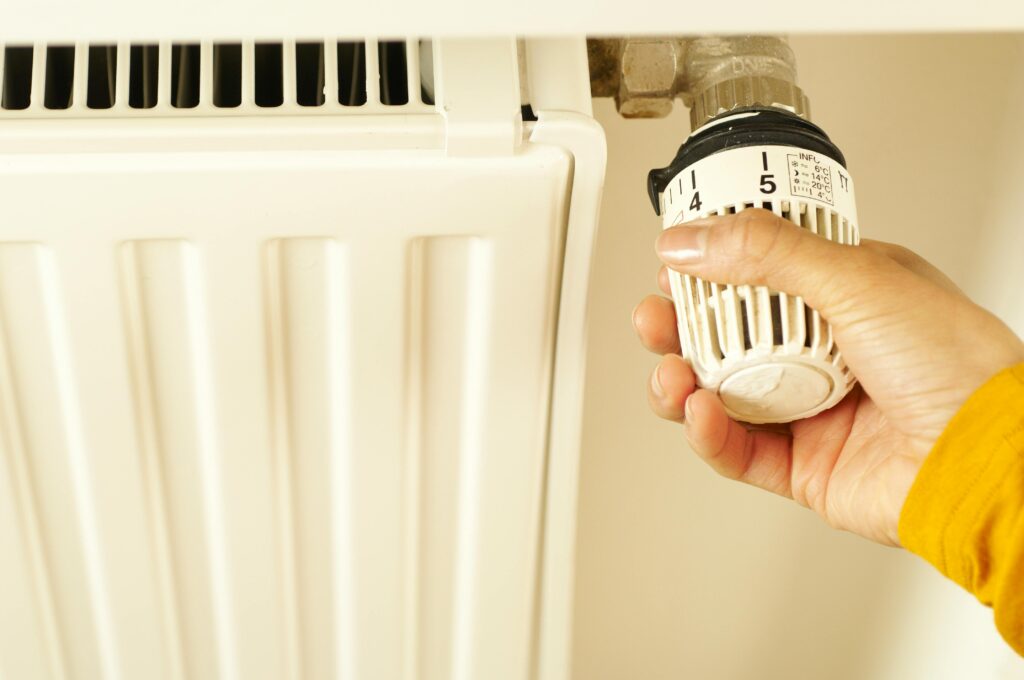 A hand turning the thermostatic valve on a white radiator