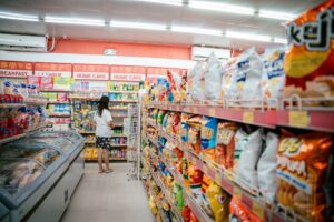 Student browsing a supermarket snack aisle with a basket