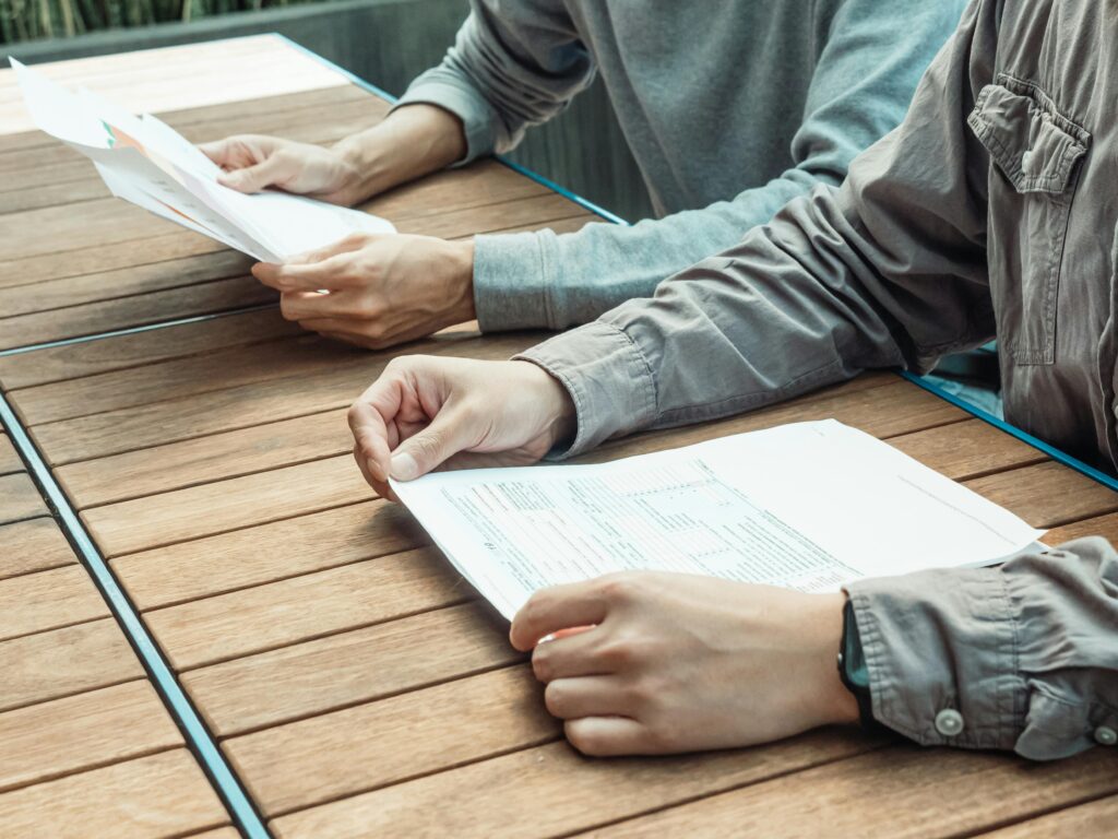 Two people reviewing business documents at an outdoor table, focused on paperwork.