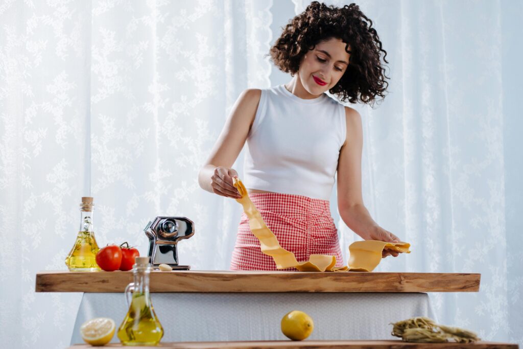 A woman joyfully preparing homemade pasta in a bright kitchen setting.