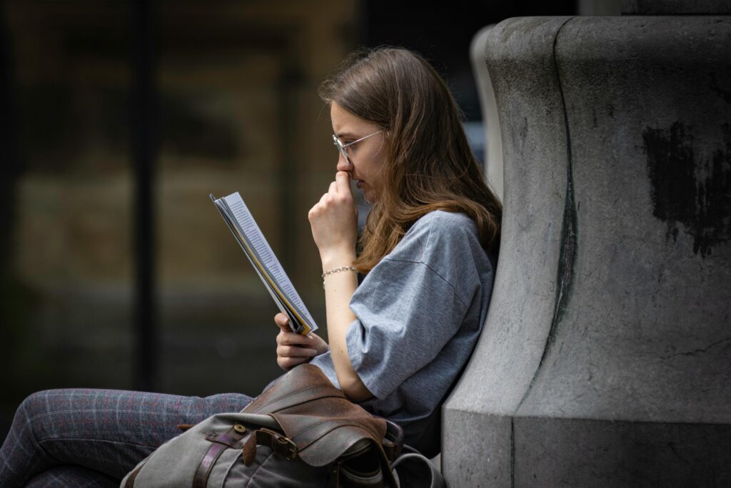 Young woman reading outdoors on a street in Lancaster, England, showcasing urban life.