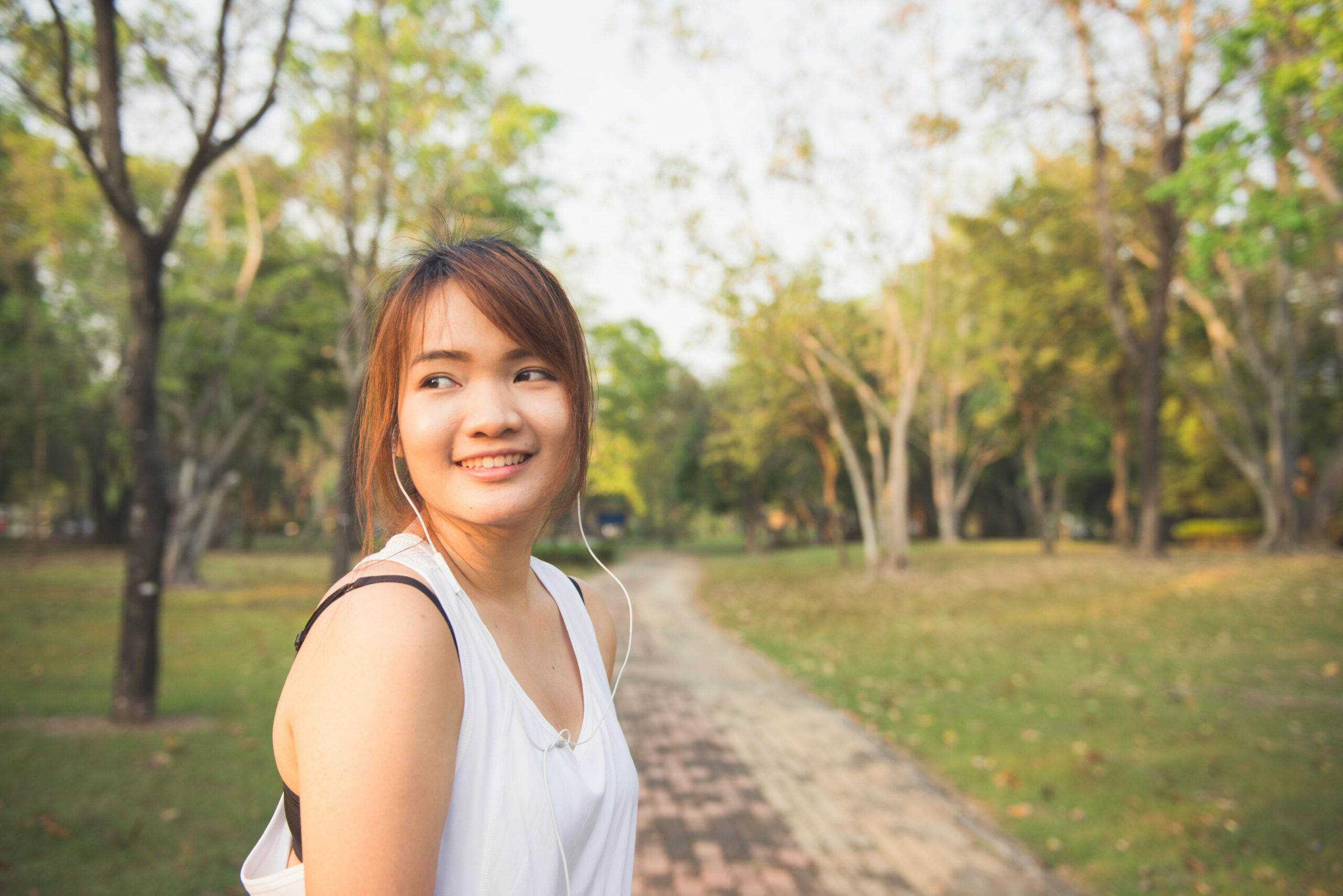 Young woman walking through a park in headphones between lectures