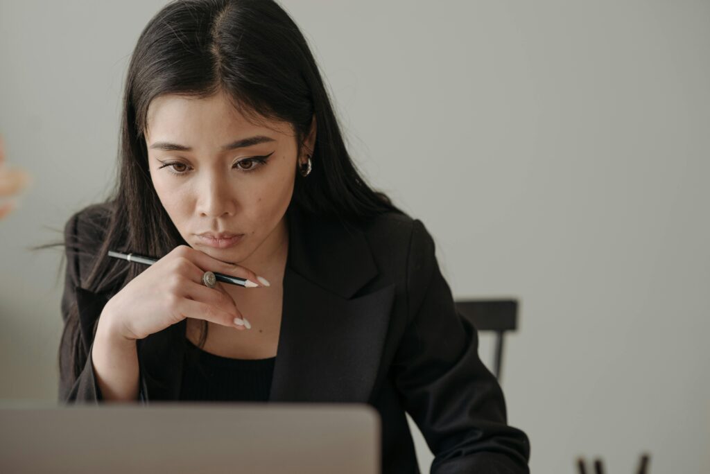Young woman working remotely, focused on laptop in home office, holding a pencil.