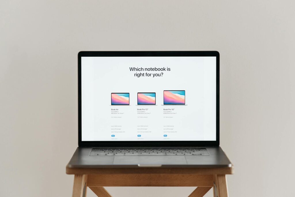Open laptop on a wooden stool displaying a three-model notebook comparison chart with prices