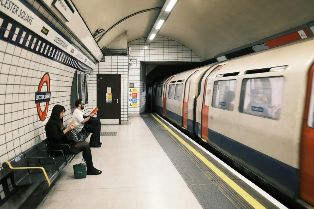 Two passengers wait on the Leicester Square London Underground platform as a Tube train arrives