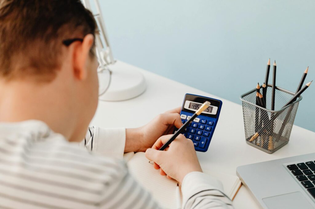 A person calculating numbers at a desk with a pencil and laptop