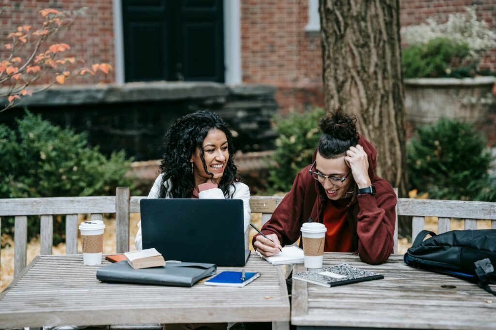 A pair of students reviewing finances on a laptop with notepads beside them