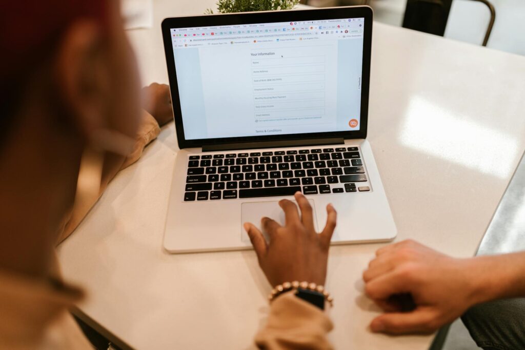 Two people working together on a laptop that displays an online application form on a wooden desk