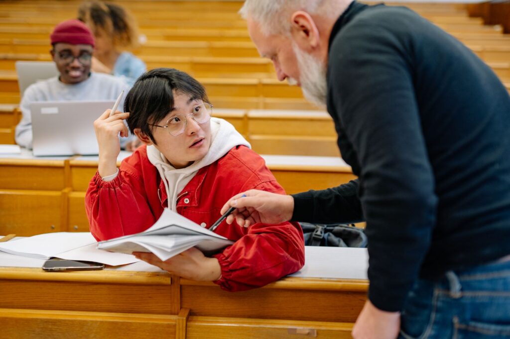 University lecturer leaning over to assist a student during a session in a tiered lecture hall