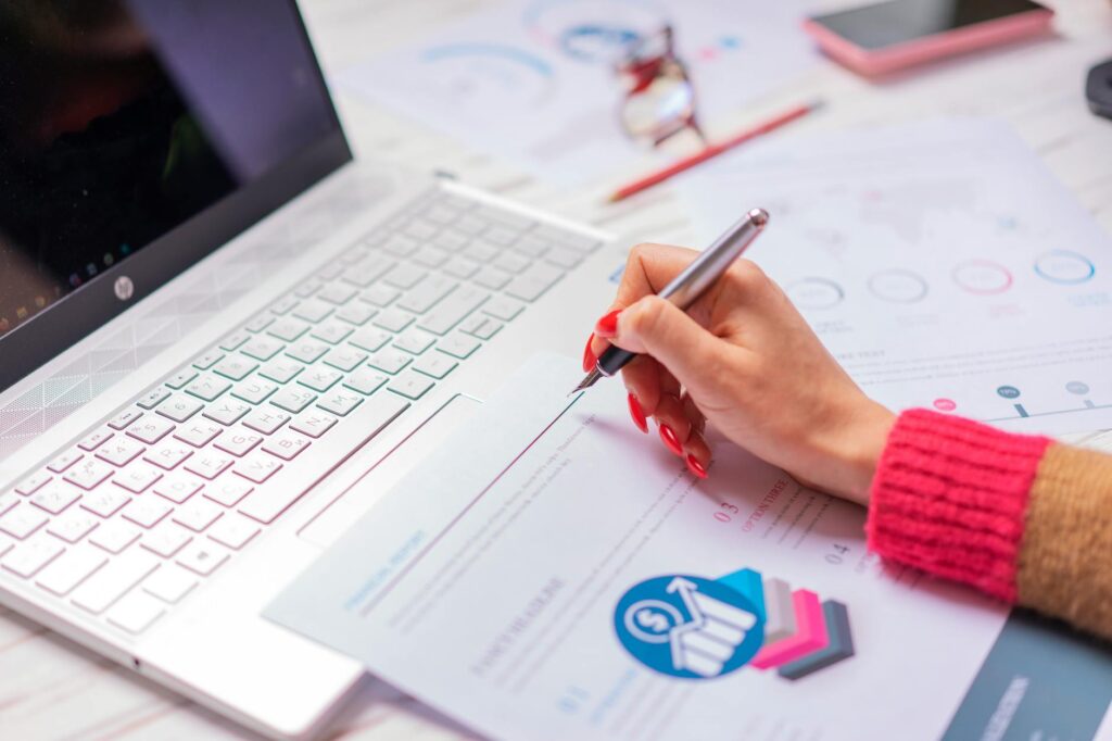 Person at a desk analysing financial figures on a laptop alongside paper documents and a pen
