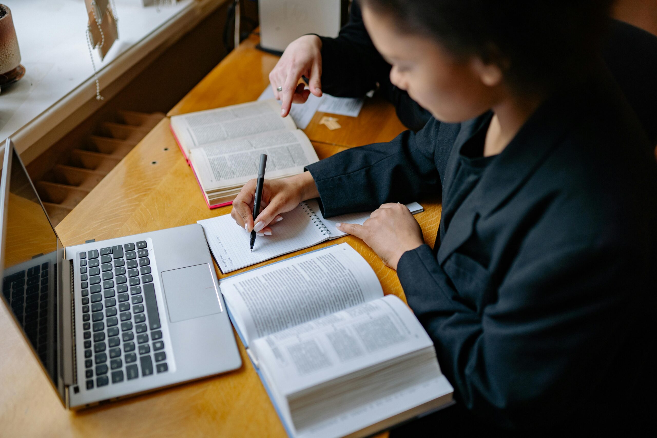 Student taking notes at a desk with a laptop and textbook open