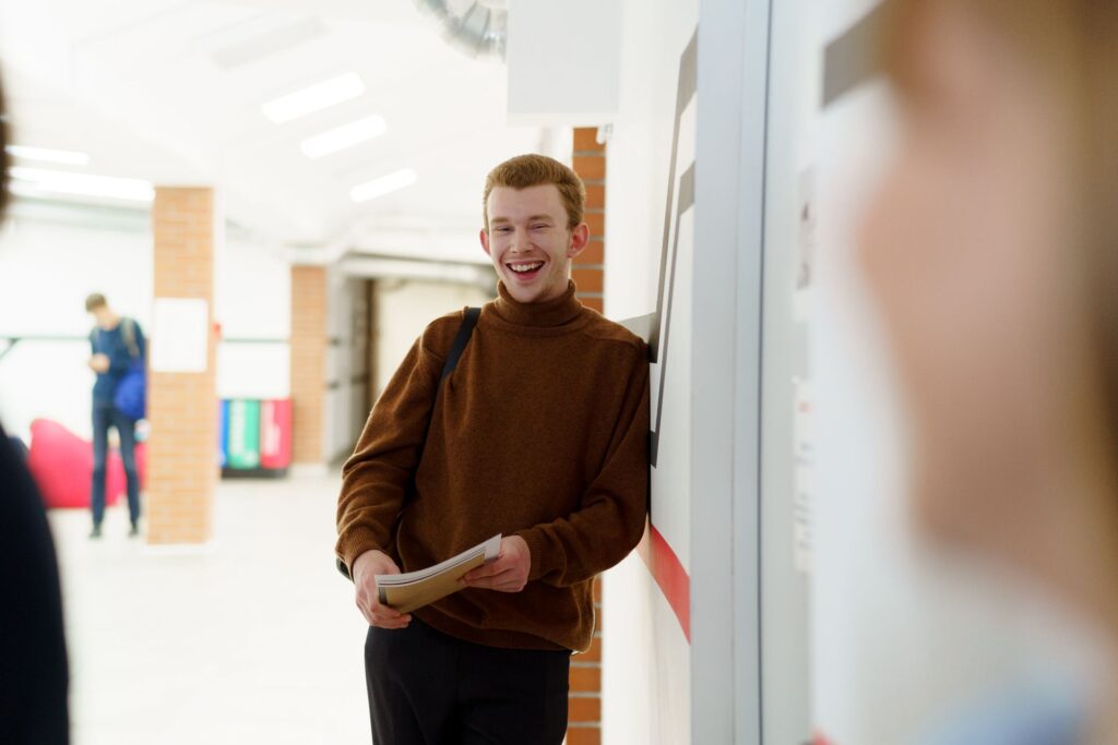 A smiling college student in a corridor holding their papers on results day