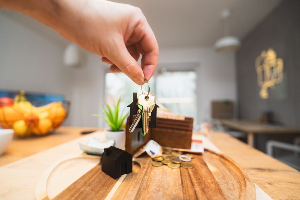 A hand holding a set of house keys above a table, representing securing student accommodation through Clearing