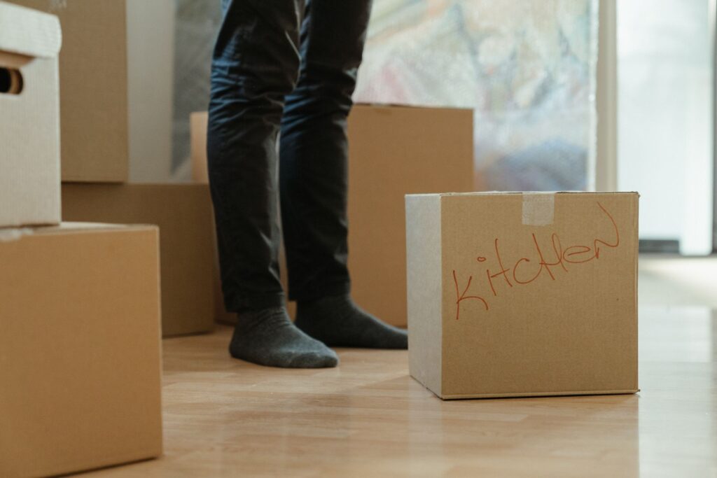 A person standing among cardboard moving boxes, one labelled kitchen, in a new flat
