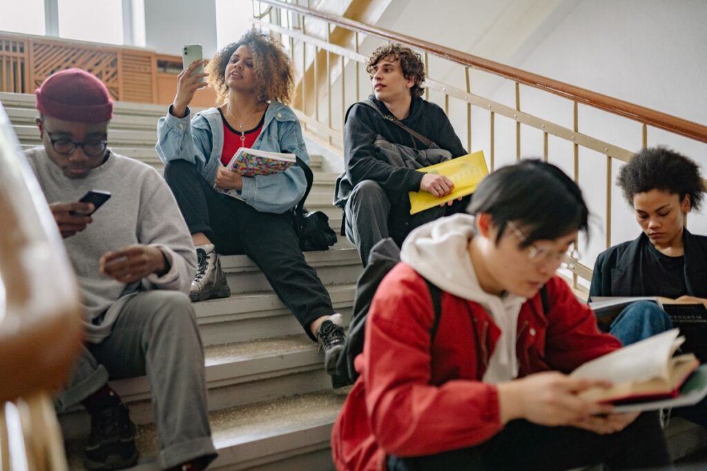 Group of students sitting on stairs, one checking a phone, deciding their next step