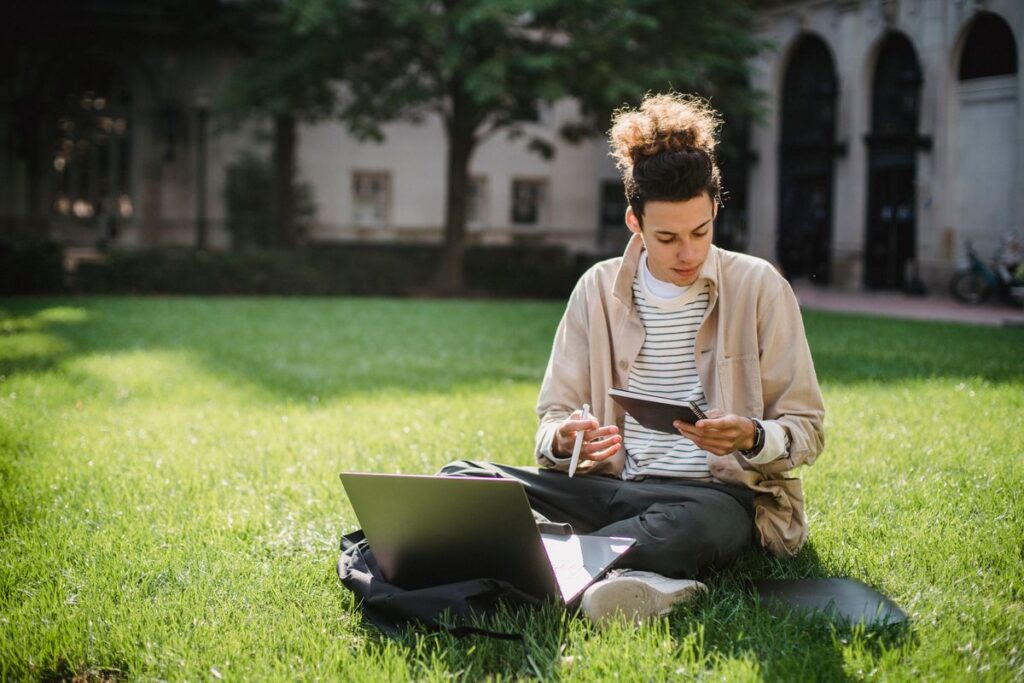 Student sitting on a university lawn researching Clearing courses on a laptop before results day