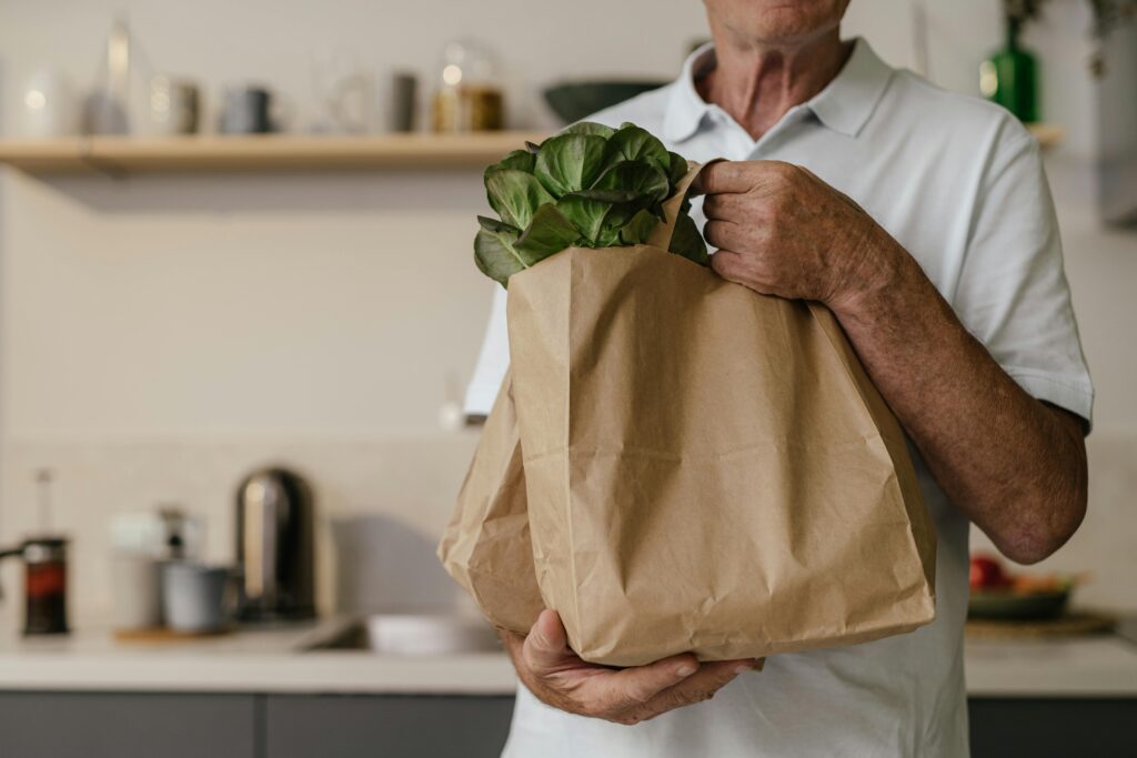Hands packing fresh vegetables into a paper grocery bag, illustrating food support options for UK students