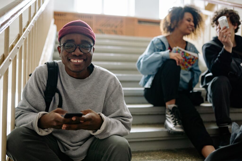 Group of happy students sitting on a college staircase checking their phones on results day.