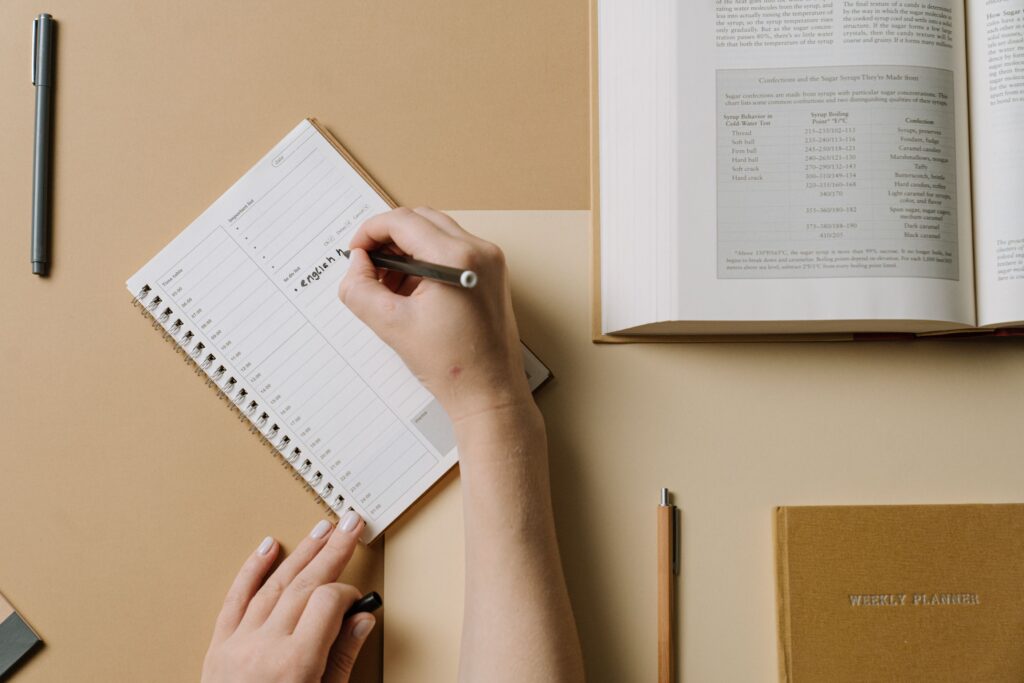 A student writing term dates into a weekly planner next to a laptop