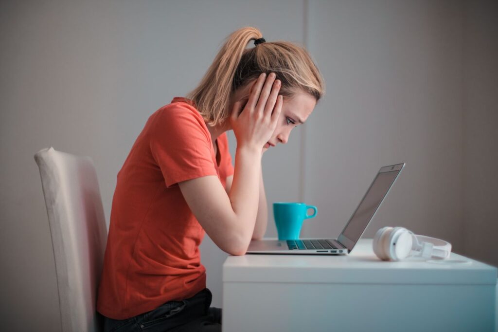 A young woman looking anxiously at a laptop while checking her results at home