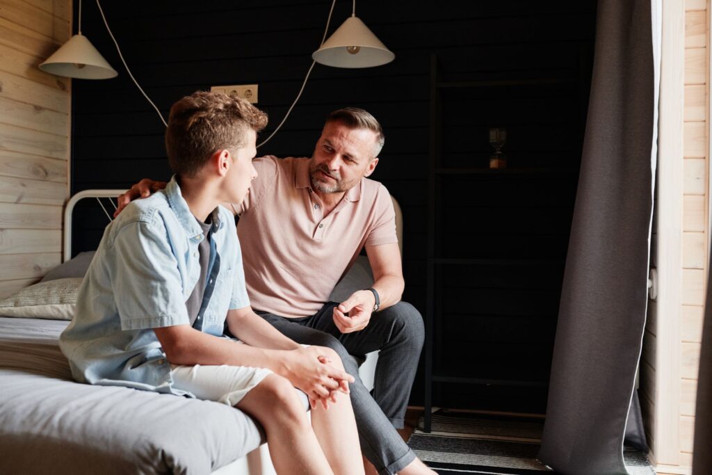 A father with his arm around his teenage son, talking calmly at home