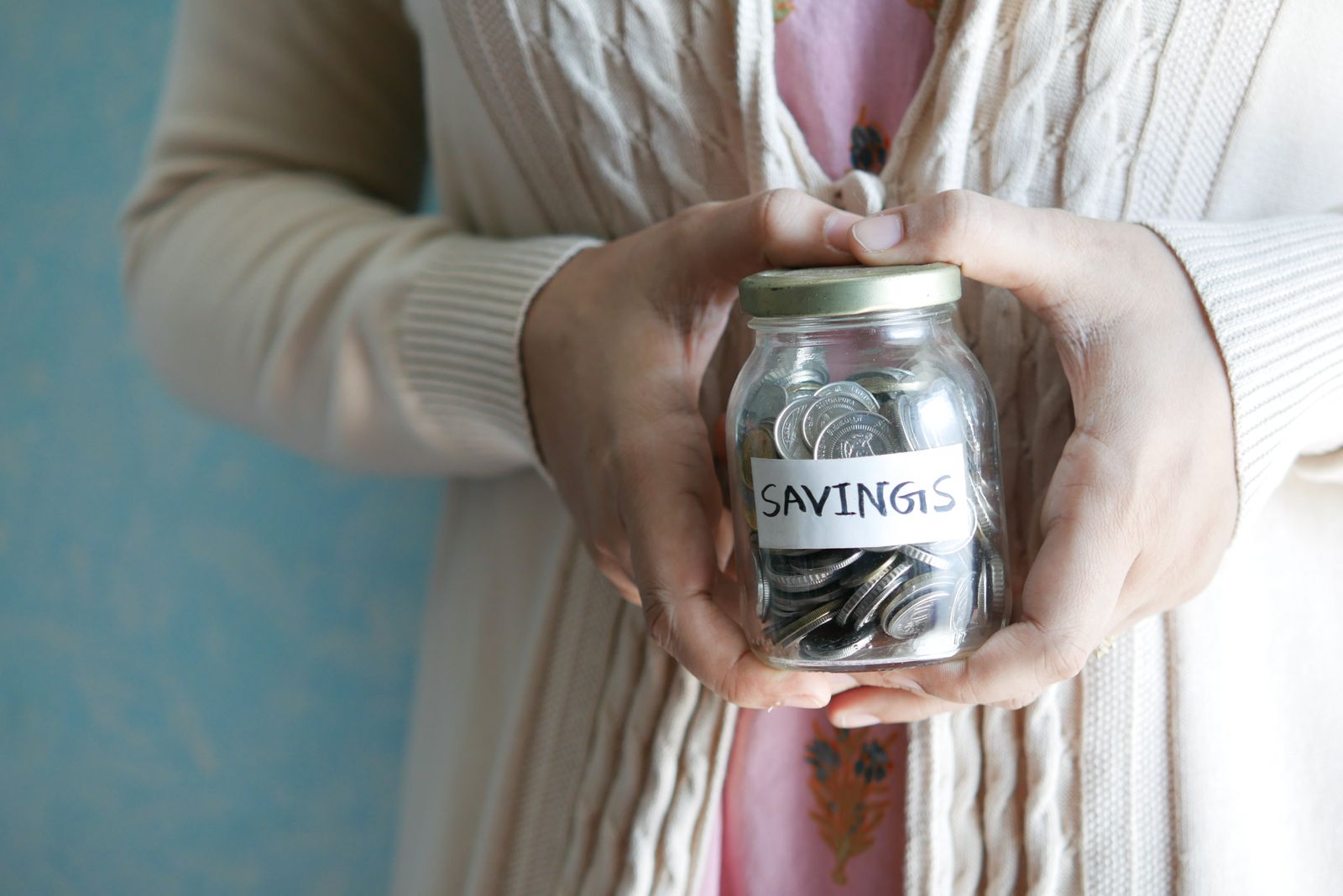 A person holding a jar labelled savings filled with coins, illustrating money saved under the interest cap
