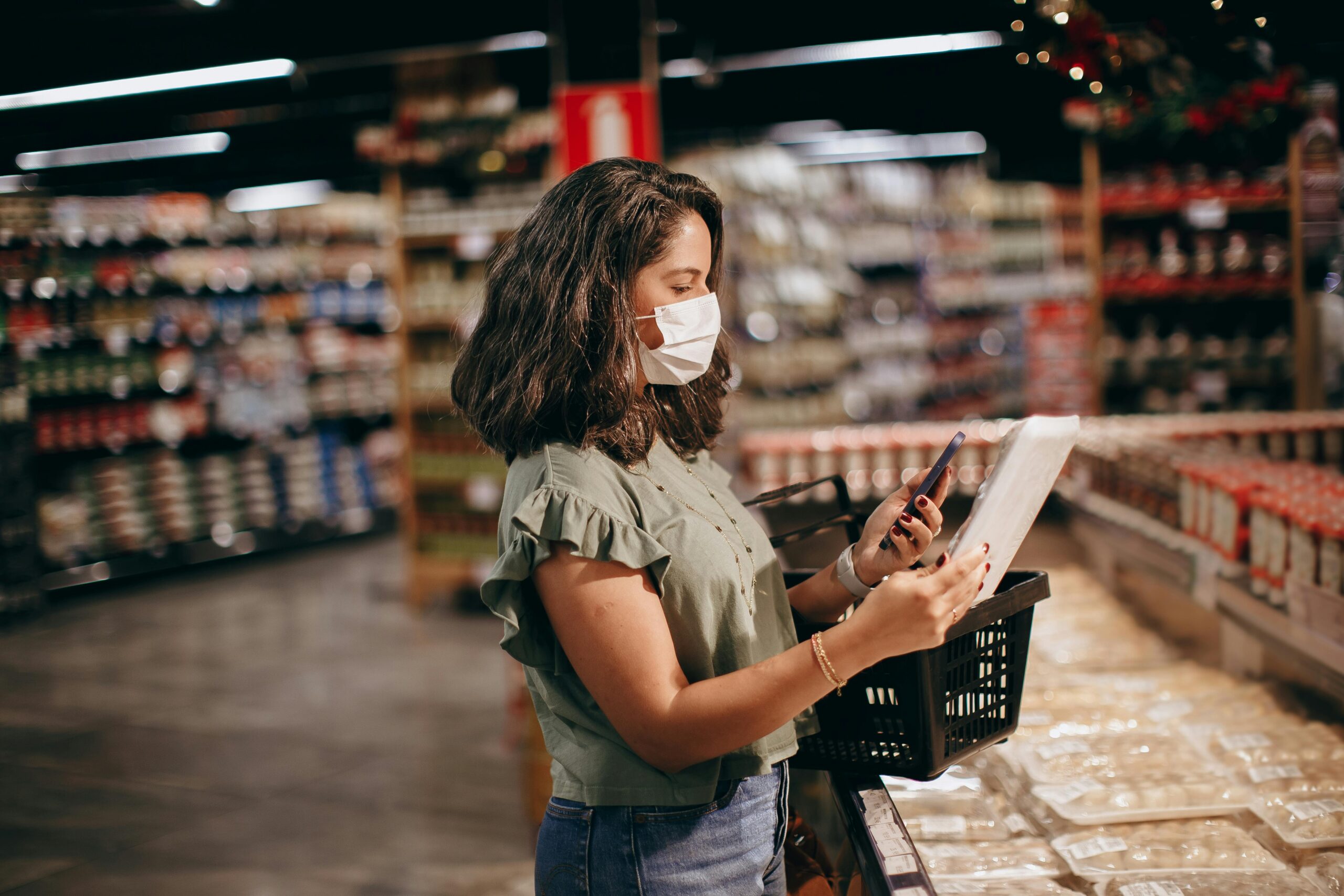 A student checking a phone in a supermarket aisle to find reduced and surplus food deals