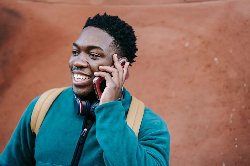 Smiling student in a green top making a phone call outdoors, backpack on, as if calling a university Clearing line on results day.