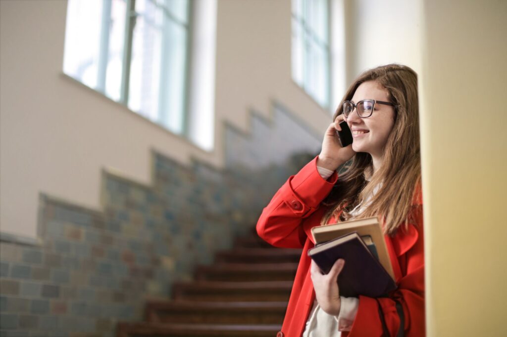 A student in an orange coat phones a university on a staircase to ask about Clearing