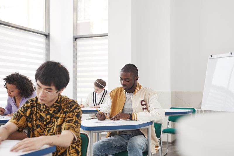 Students writing an AQA exam at desks in a bright hall