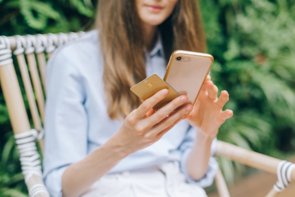 Young woman holding a bank card in one hand while using her smartphone