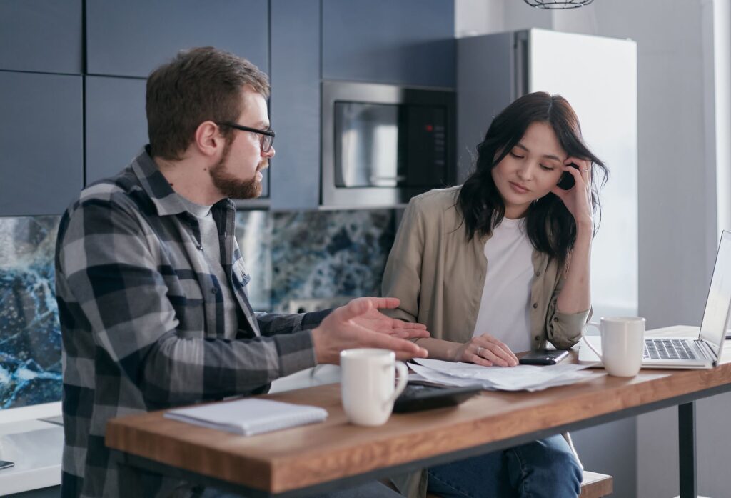 Two people in a tense discussion over paperwork and a calculator at a kitchen table