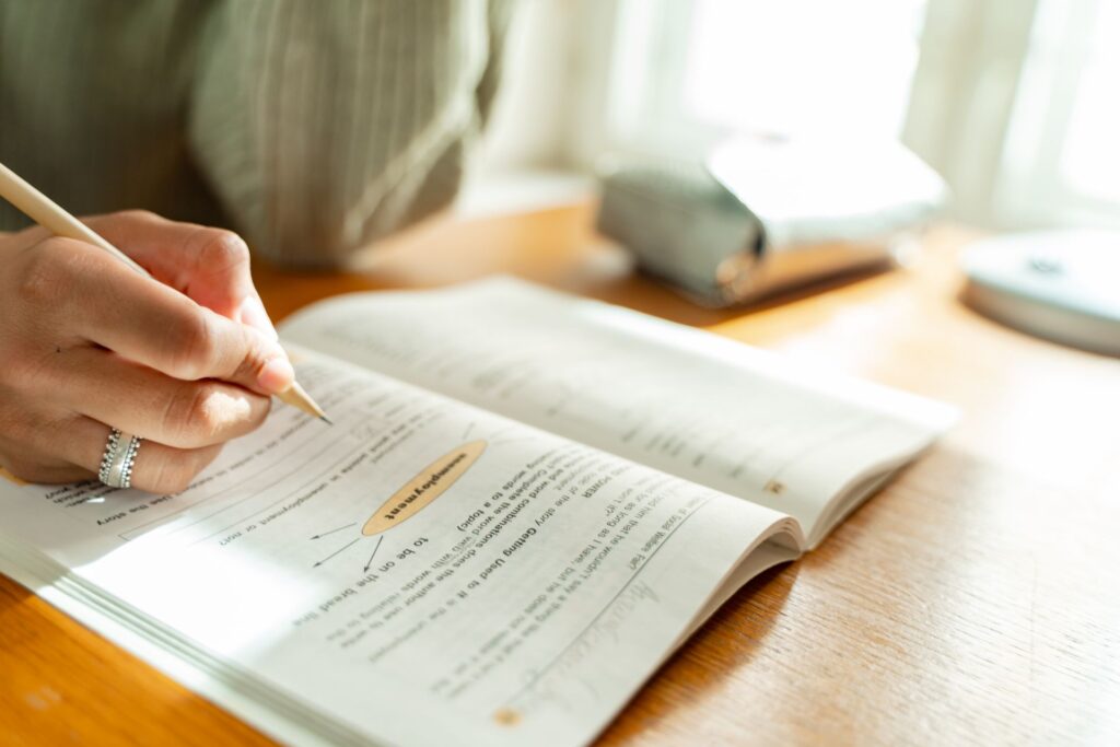 Student working through practice questions in a workbook with a pencil at a sunlit desk