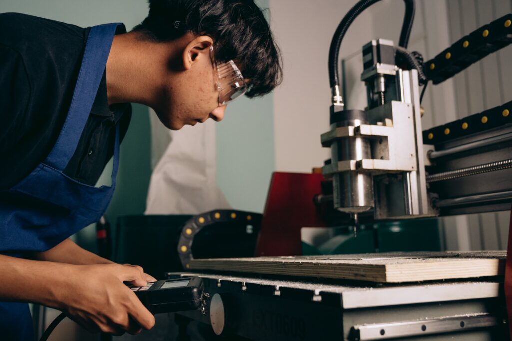 Young apprentice wearing safety goggles operating a CNC milling machine