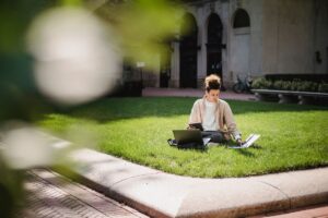 A student working on a laptop on a campus lawn