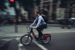 A man with a backpack rides a bicycle through a busy, blurred street in London, capturing dynamic city life.