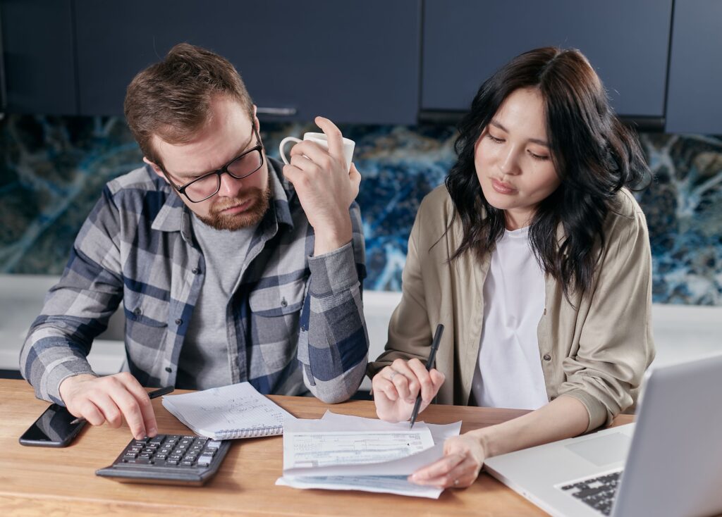 Couple working through household bills at a kitchen table with a calculator and laptop
