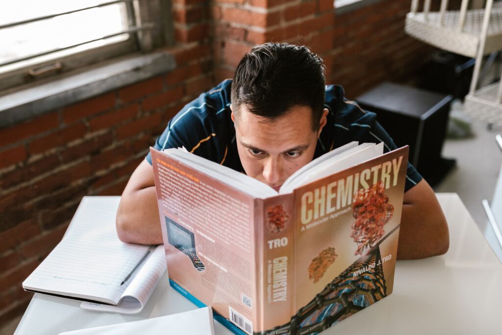 Mature student reading a chemistry textbook closely at a desk by a brick wall