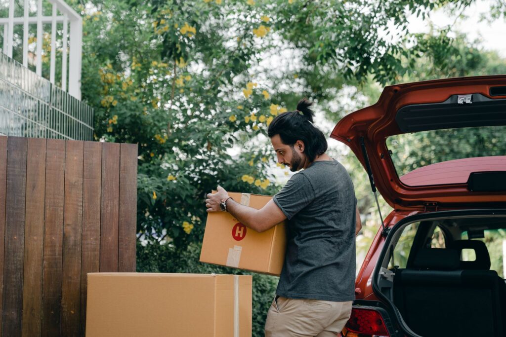 Young man loading cardboard boxes into the open boot of a car on moving day