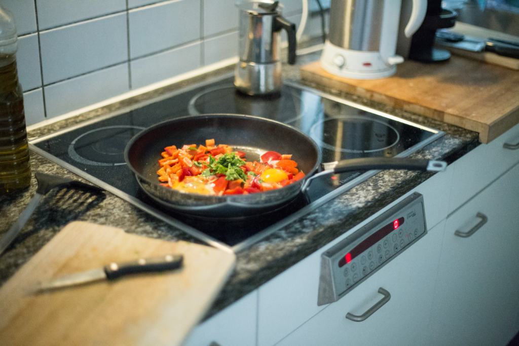 Frying pan with peppers and egg cooking on an induction hob in a small kitchen