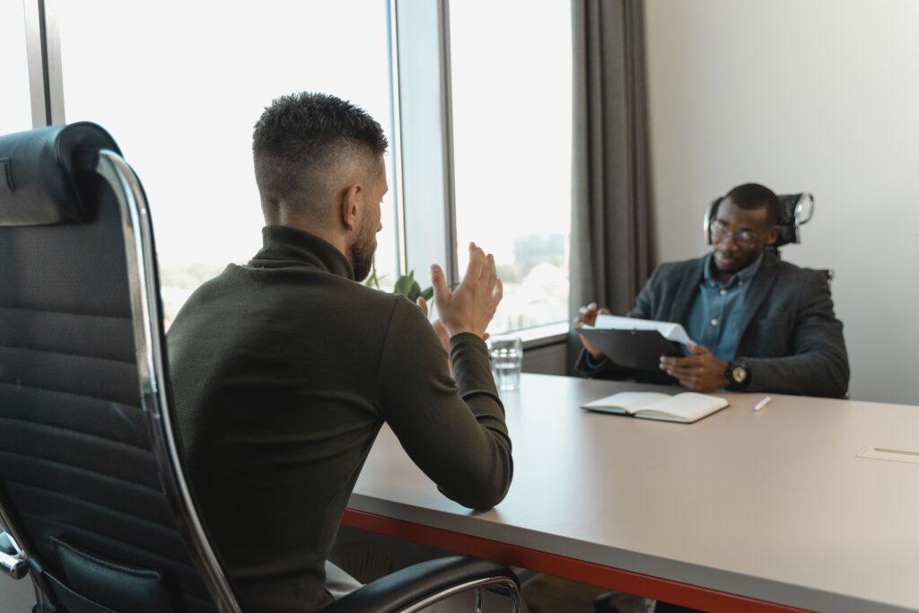 A candidate talking across a boardroom table while an interviewer reads through their application.