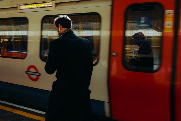 Man walks past a moving train on a London Underground platform during the day.