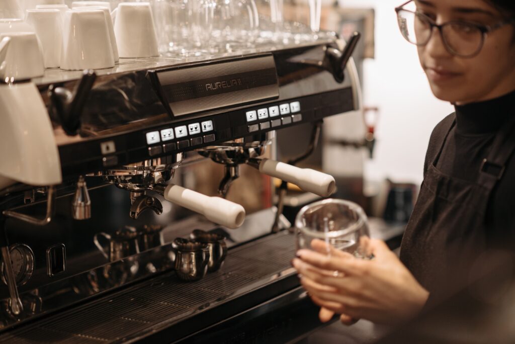 Young barista in glasses working at an espresso machine in a cafe