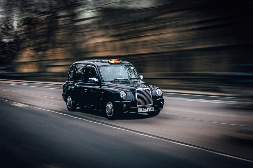 Black cab with its taxi light on driving along a tree-lined UK street