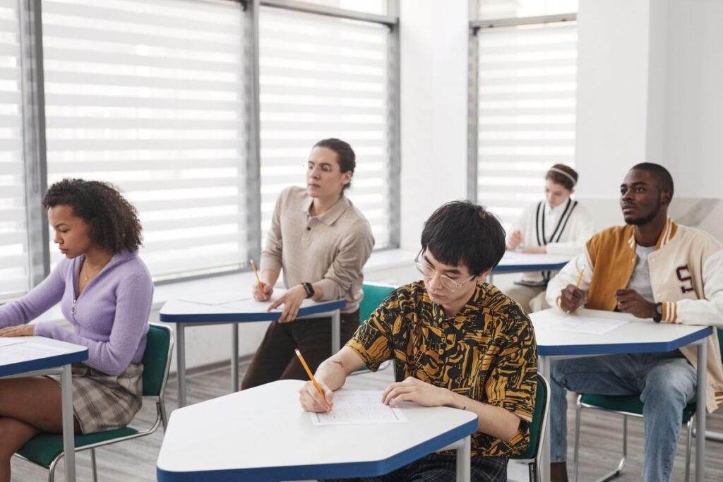Students writing exam papers at desks in a bright exam hall